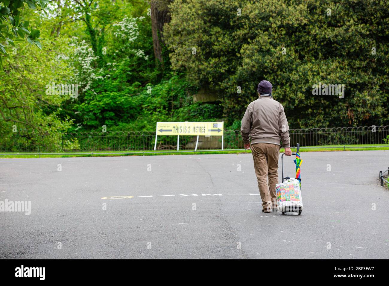 Dublin, Ireland. May 2020. Man walks through the St Stephen`s Green Park signposted with yellow Covid-19 social distancing safety notices. Stock Photo